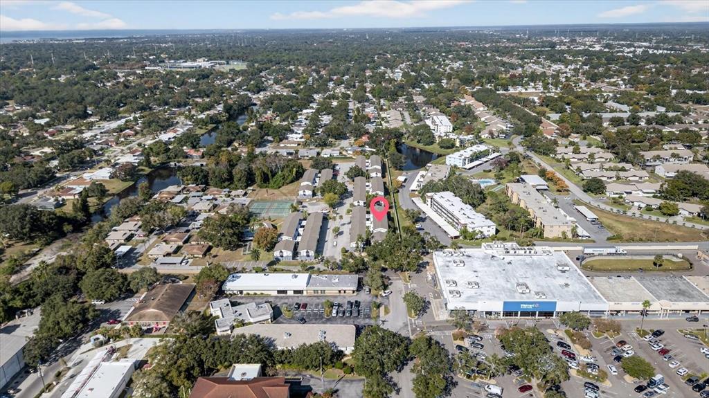 This aerial view shows a residential apartment complex with a marked unit near a shopping center — 1146 KING ARTHUR COURT UNIT 110, DUNEDIN, FL