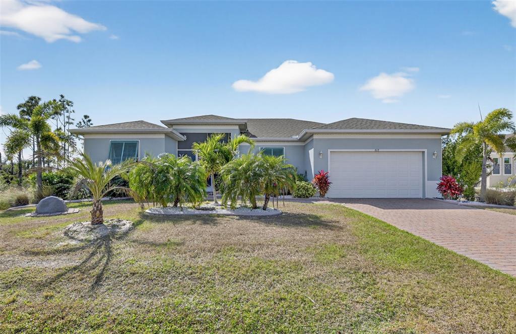 A single-story house with a light gray exterior, a two-car garage, and palm tree landscaping — 8117 THRUSO ROAD, PORT CHARLOTTE, FL