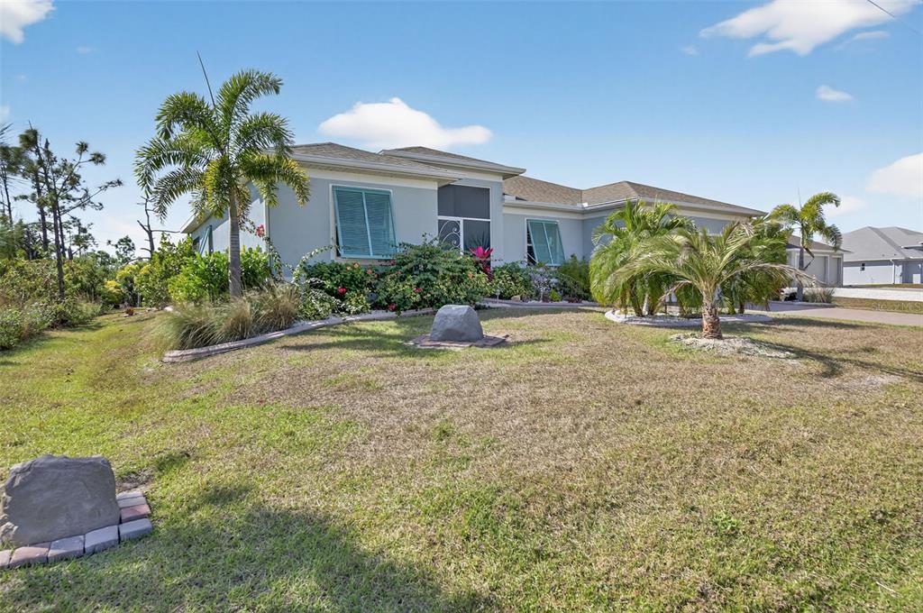 A single-story house with light-colored stucco walls, teal shutters, and palm trees in the yard — 8117 THRUSO ROAD, PORT CHARLOTTE, FL