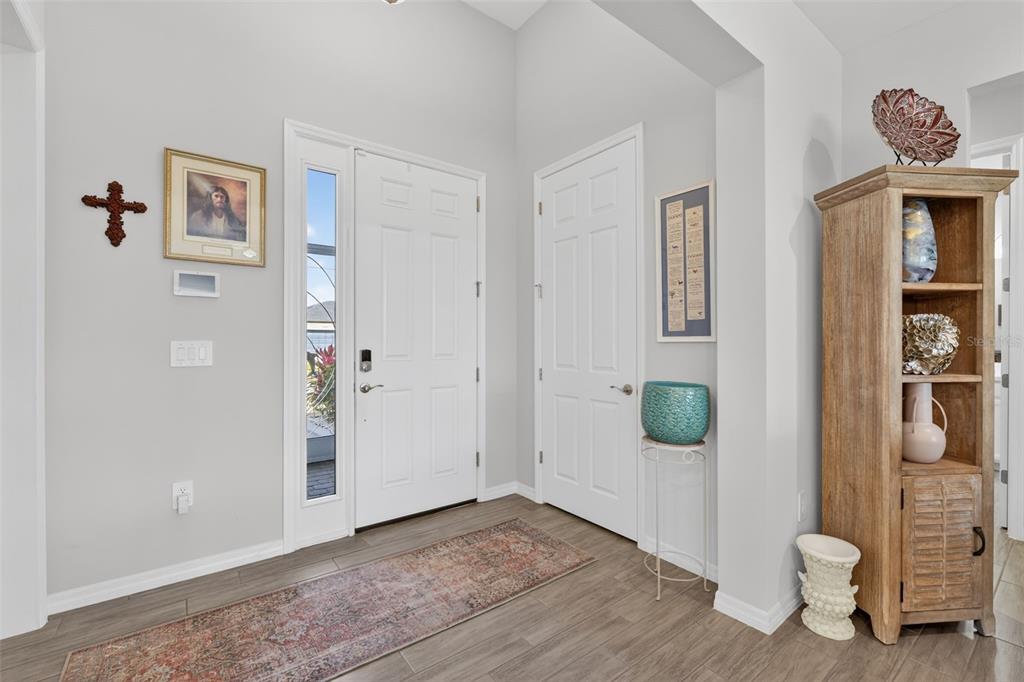 An entryway features a white front door, light gray walls, wood-look tile flooring, and a bookshelf — 8117 THRUSO ROAD, PORT CHARLOTTE, FL