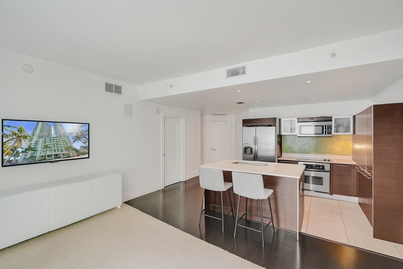 A modern kitchen with a center island and bar stools opens into a living area — 1900 N Bayshore Dr # 3207, Miami FL 33132, MIAMI, FL