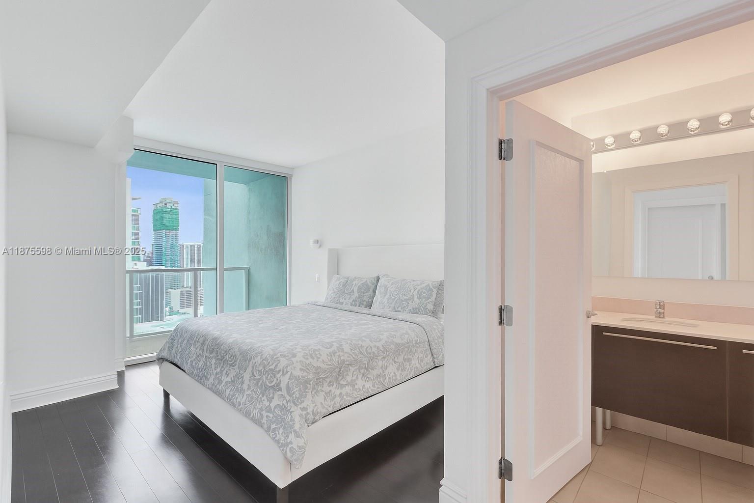 A bedroom with dark wood floors and a balcony overlooks a city skyline near a bathroom — 1900 N Bayshore Dr # 3207, Miami FL 33132, MIAMI, FL