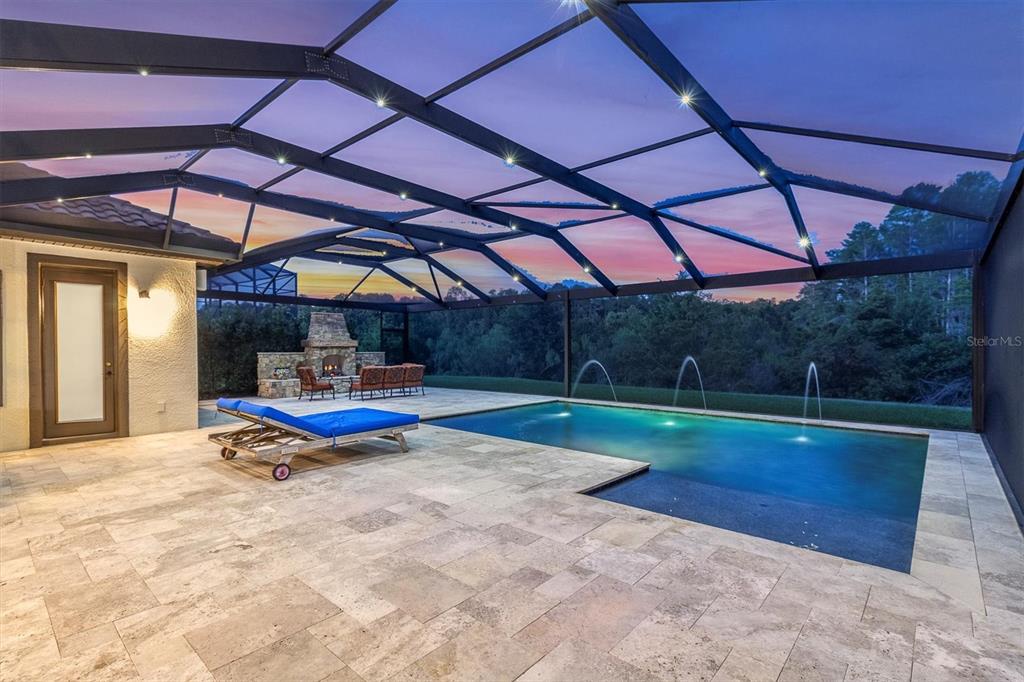 A screened-in patio features a swimming pool with fountains, stone pavers, and an outdoor fireplace — 3100 BARBOUR TRAIL, ODESSA, FL