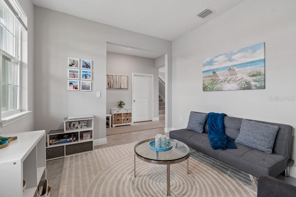 A living room features a gray sofa, a glass coffee table, and light-colored tile flooring — 116 BRIGHT IBIS AVENUE, APOLLO BEACH, FL