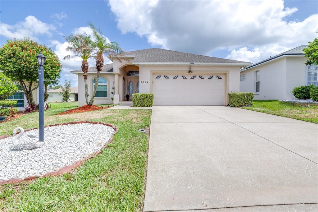 A single-story house with a beige stucco exterior, a two-car garage, and a palm tree — 7024 BENDELOW DRIVE, LAKELAND, FL