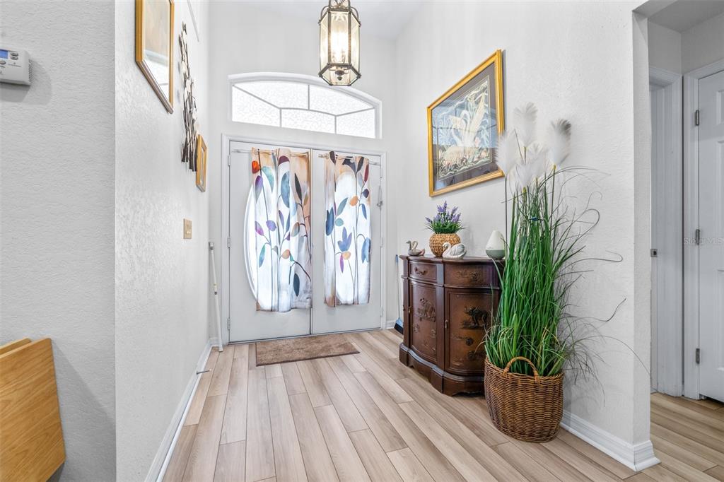 An entryway features light wood-look flooring, a dark wood cabinet, and double front doors — 7024 BENDELOW DRIVE, LAKELAND, FL