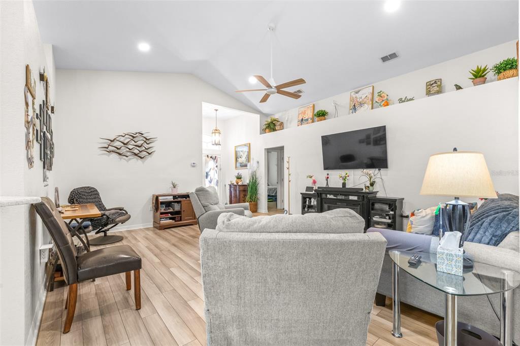 A living room features vaulted ceilings, wood-look flooring, a ceiling fan, and a wall-mounted television — 7024 BENDELOW DRIVE, LAKELAND, FL
