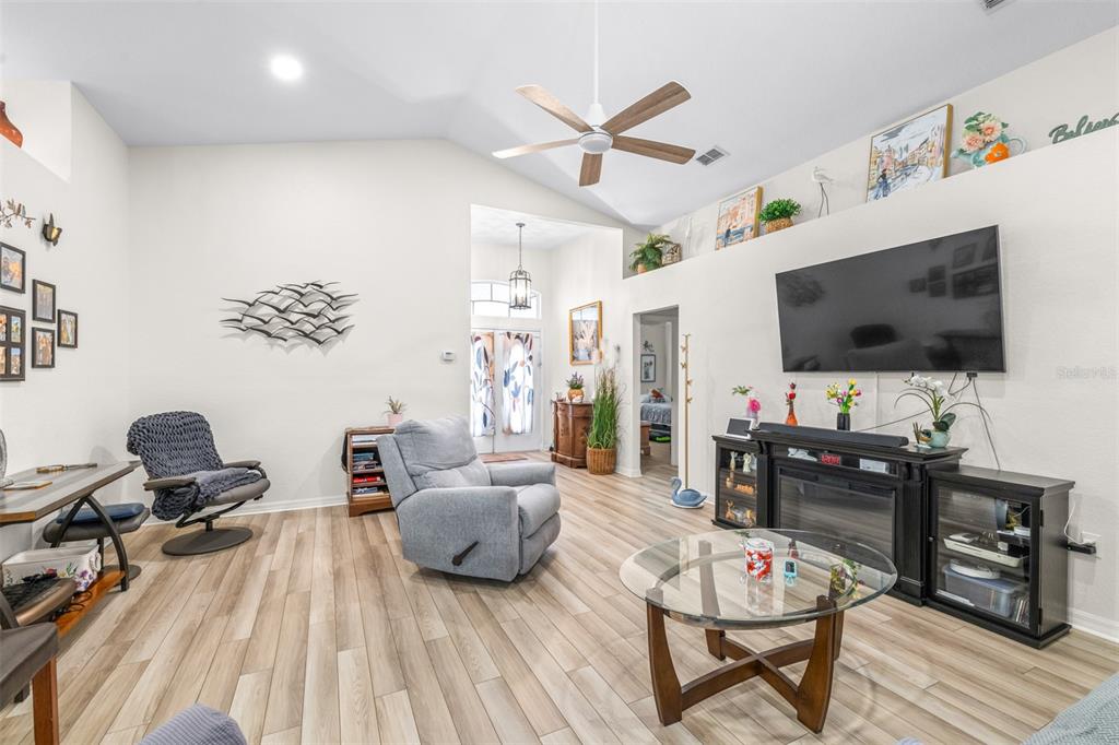 A living room features vaulted ceilings, light wood-look flooring, a ceiling fan, and a television — 7024 BENDELOW DRIVE, LAKELAND, FL