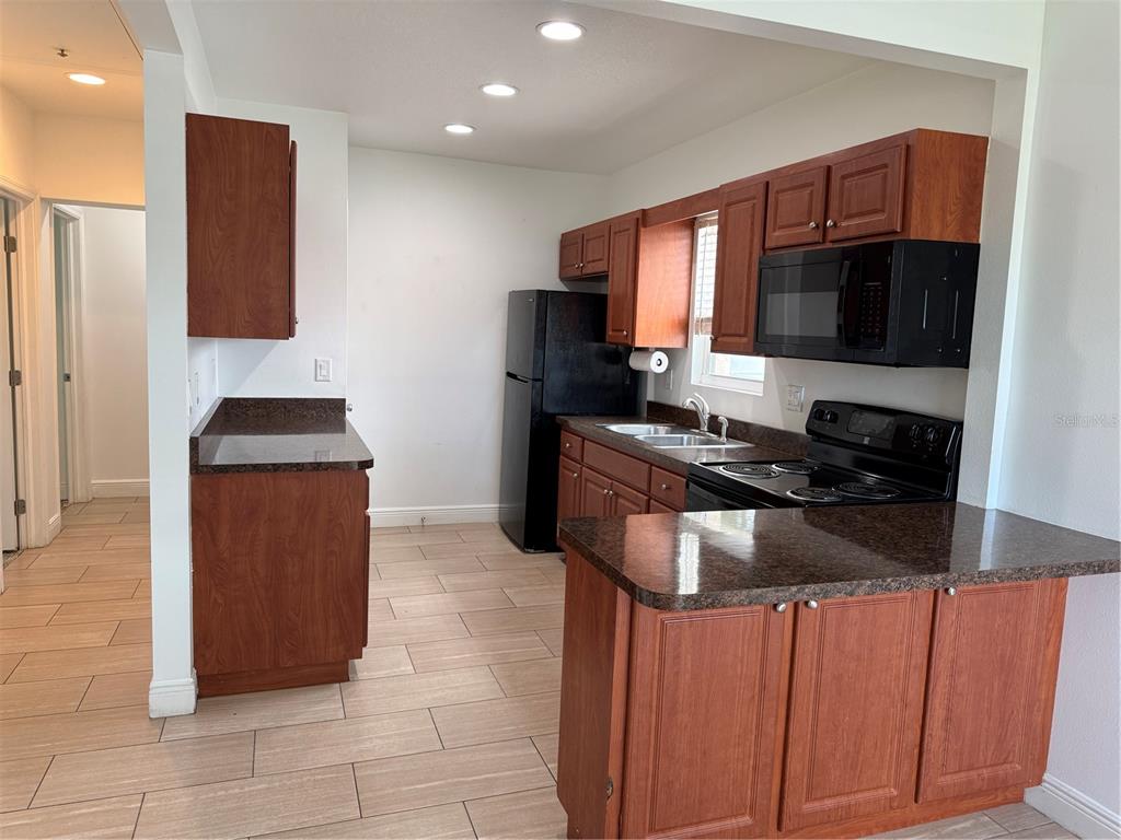 A kitchen features wood cabinets, dark countertops, black appliances, and light-colored tile flooring — 1026 36TH AVENUE E, ELLENTON, FL