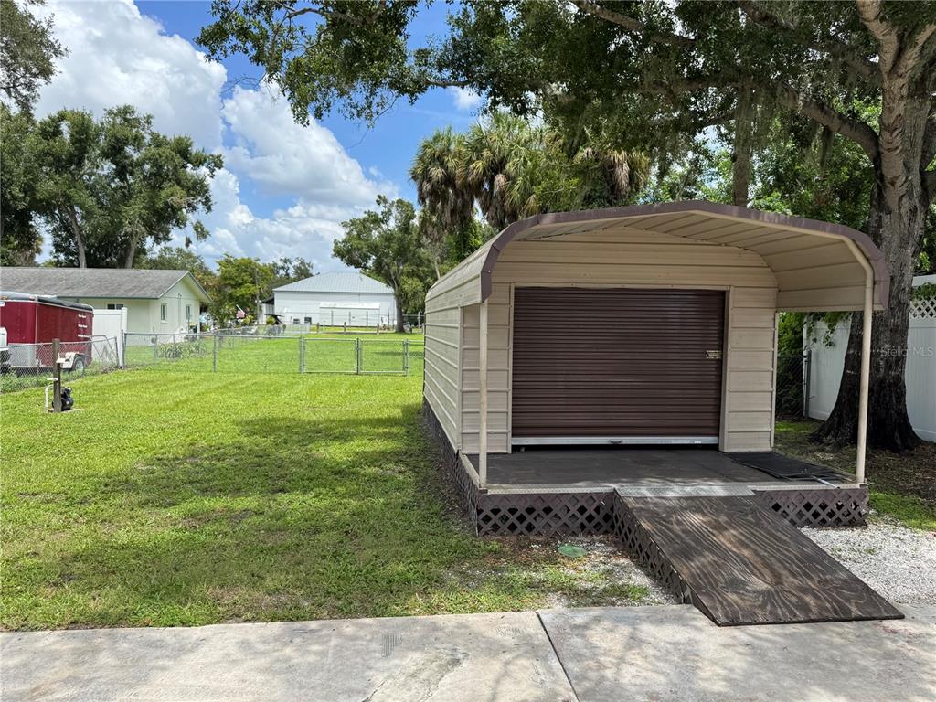 A metal storage shed with a roll-up door sits on a grassy lot — 1026 36TH AVENUE E, ELLENTON, FL