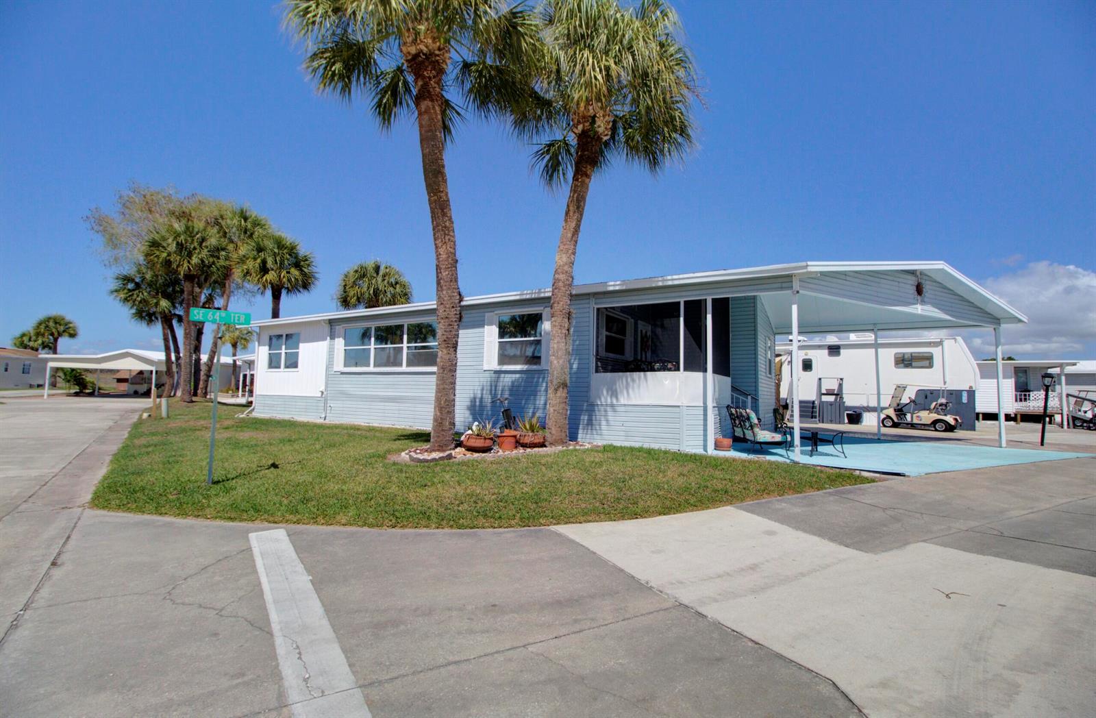 A light blue mobile home features a carport, a screened porch, and two tall palm trees — 5395 SE 64th Terrace, Okeechobee FL 34974, OKEECHOBEE, FL