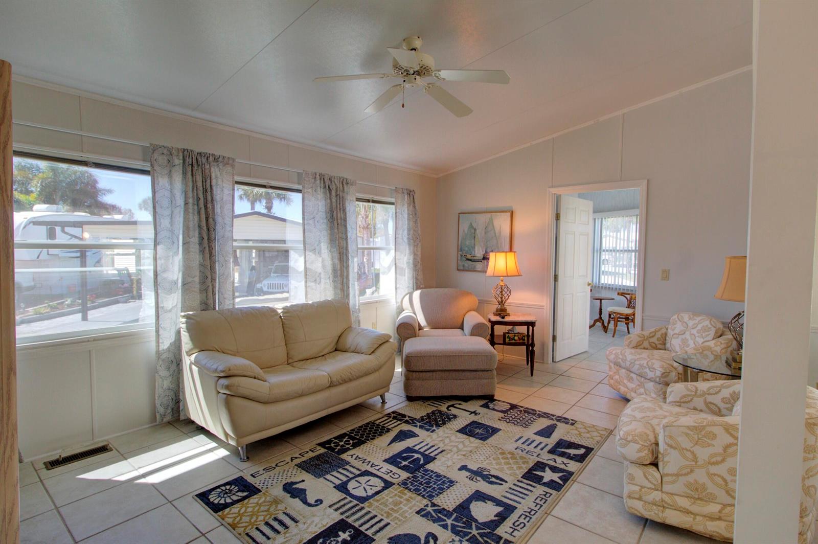 A living room features a white sofa, patterned armchairs, a nautical rug, and tile flooring — 5395 SE 64th Terrace, Okeechobee FL 34974, OKEECHOBEE, FL