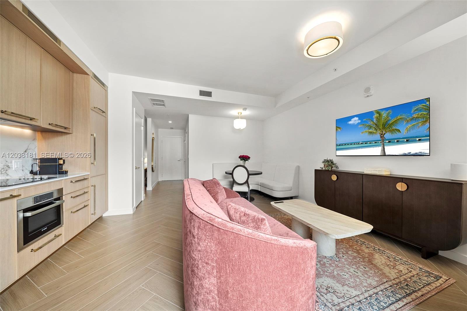 A modern living room features a pink curved sofa, light wood cabinetry, and a television — 2700 NW 2nd Ave # 532, Miami FL 33127, MIAMI, FL