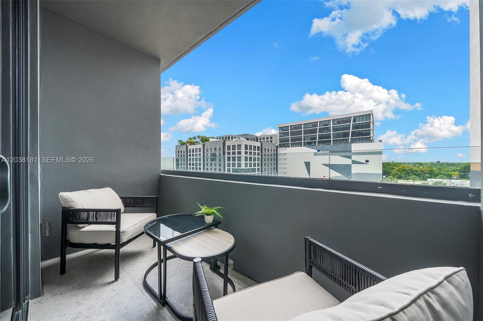 A balcony features two chairs, a small table, and a glass railing overlooking city buildings — 2700 NW 2nd Ave # 532, Miami FL 33127, MIAMI, FL
