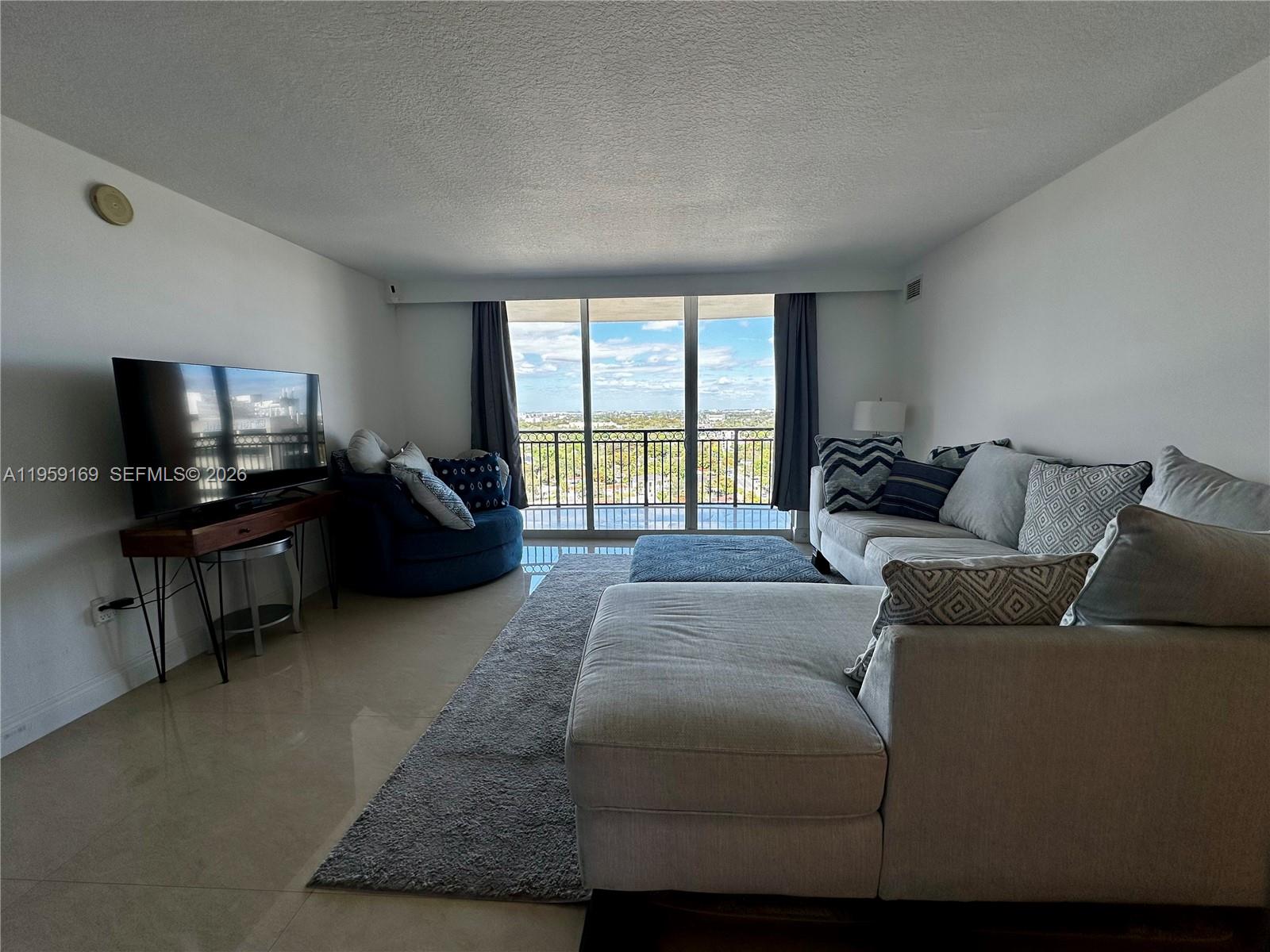 A living room features a sectional sofa, a blue chair, and a balcony with views — 3232 SW 22nd Ter # 1604, Miami FL 33145, MIAMI, FL