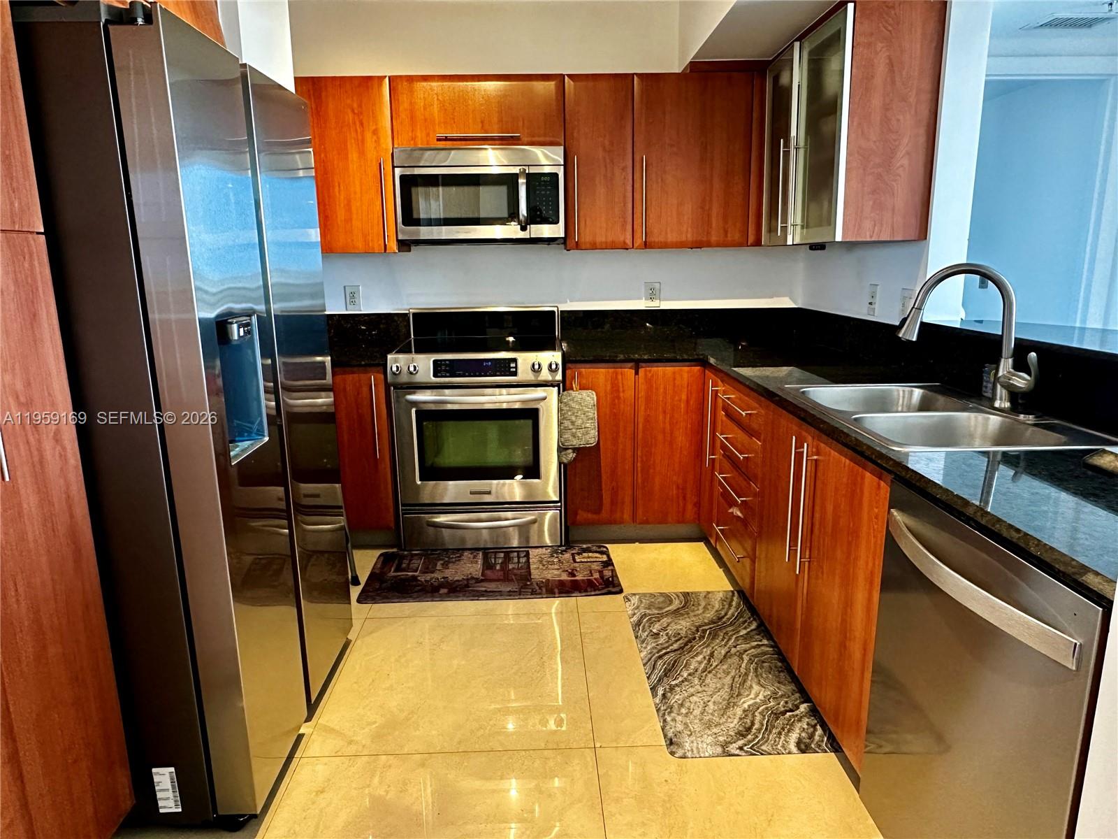 A kitchen features wood cabinets, stainless steel appliances, black countertops, and light-colored tile flooring — 3232 SW 22nd Ter # 1604, Miami FL 33145, MIAMI, FL