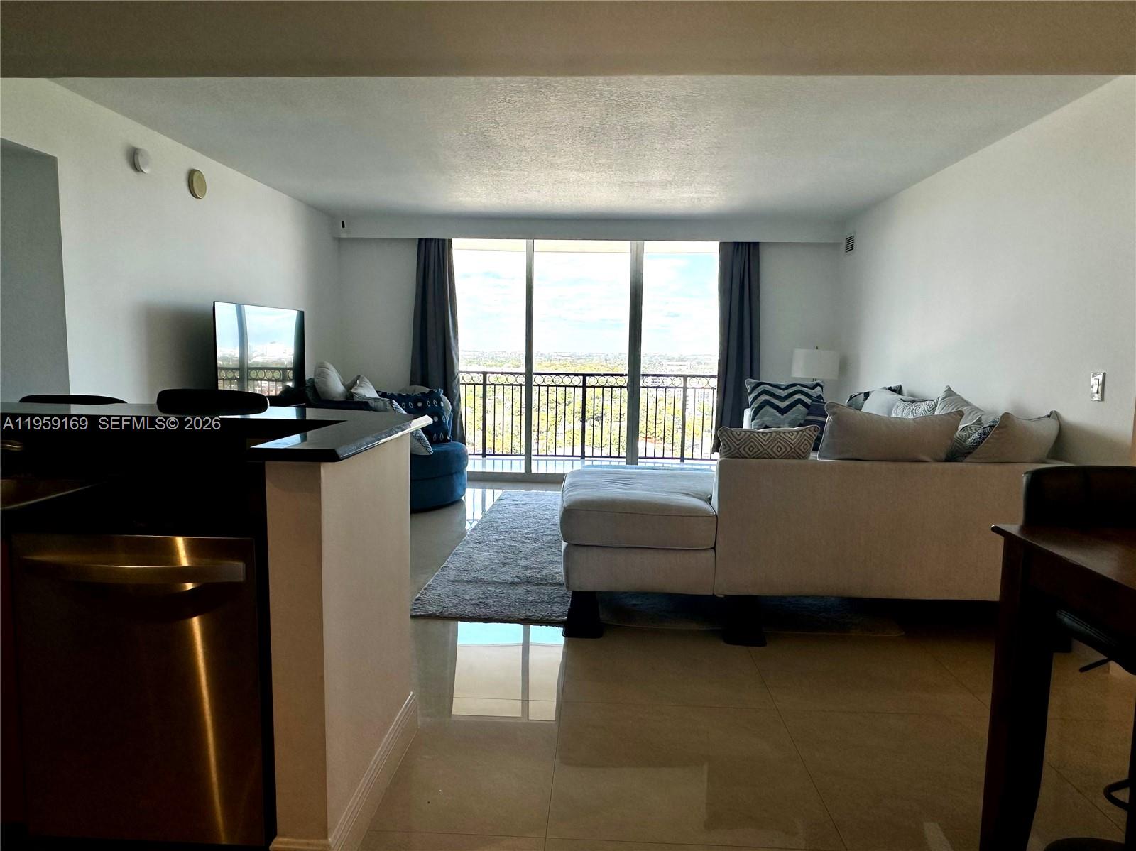 A living room features a sectional sofa, a balcony with a view, and tile flooring — 3232 SW 22nd Ter # 1604, Miami FL 33145, MIAMI, FL