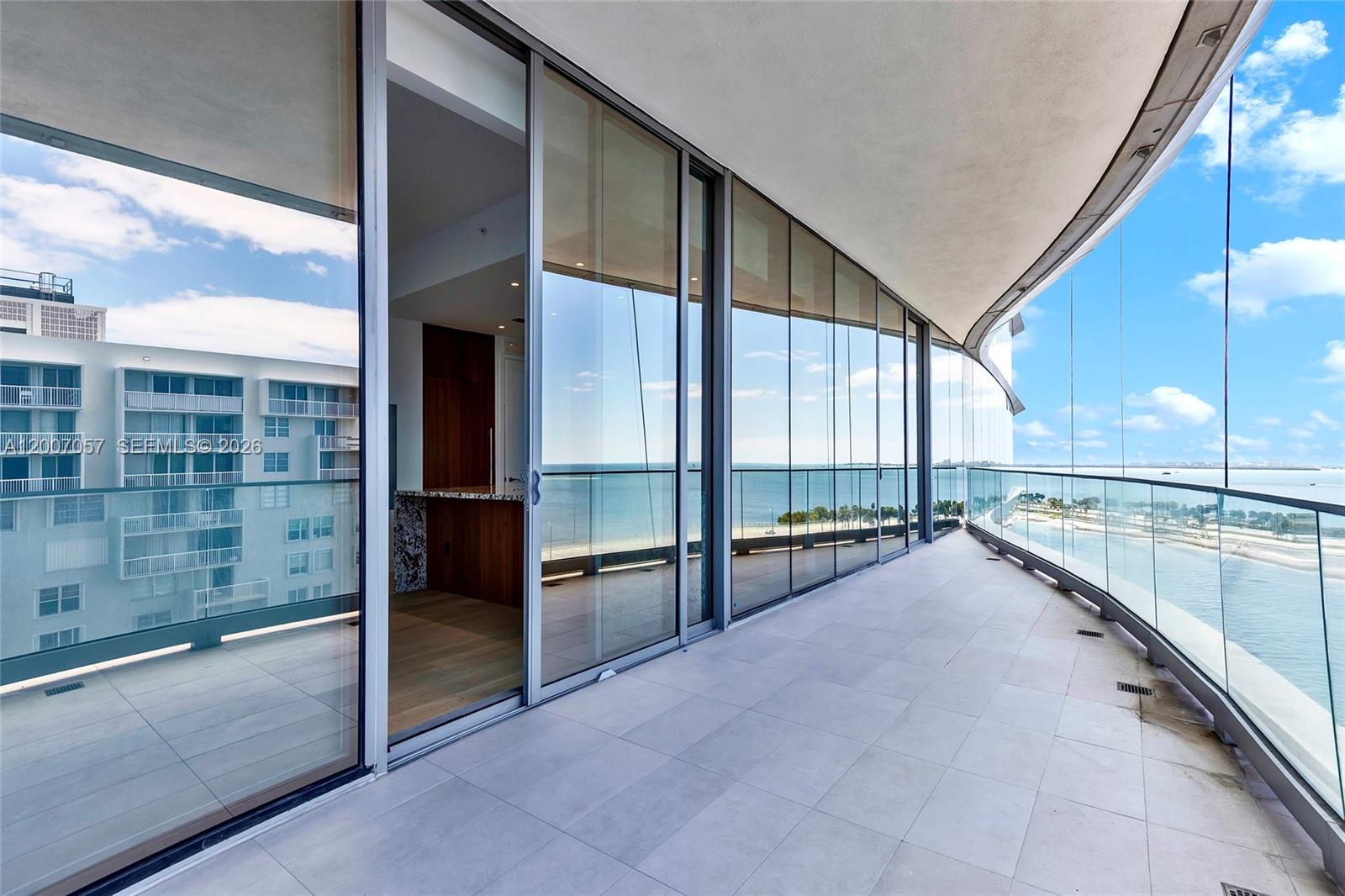 A curved balcony with glass railings overlooks the ocean and a neighboring building — 175 SE 25 Road # 803, Miami FL 33129, MIAMI, FL