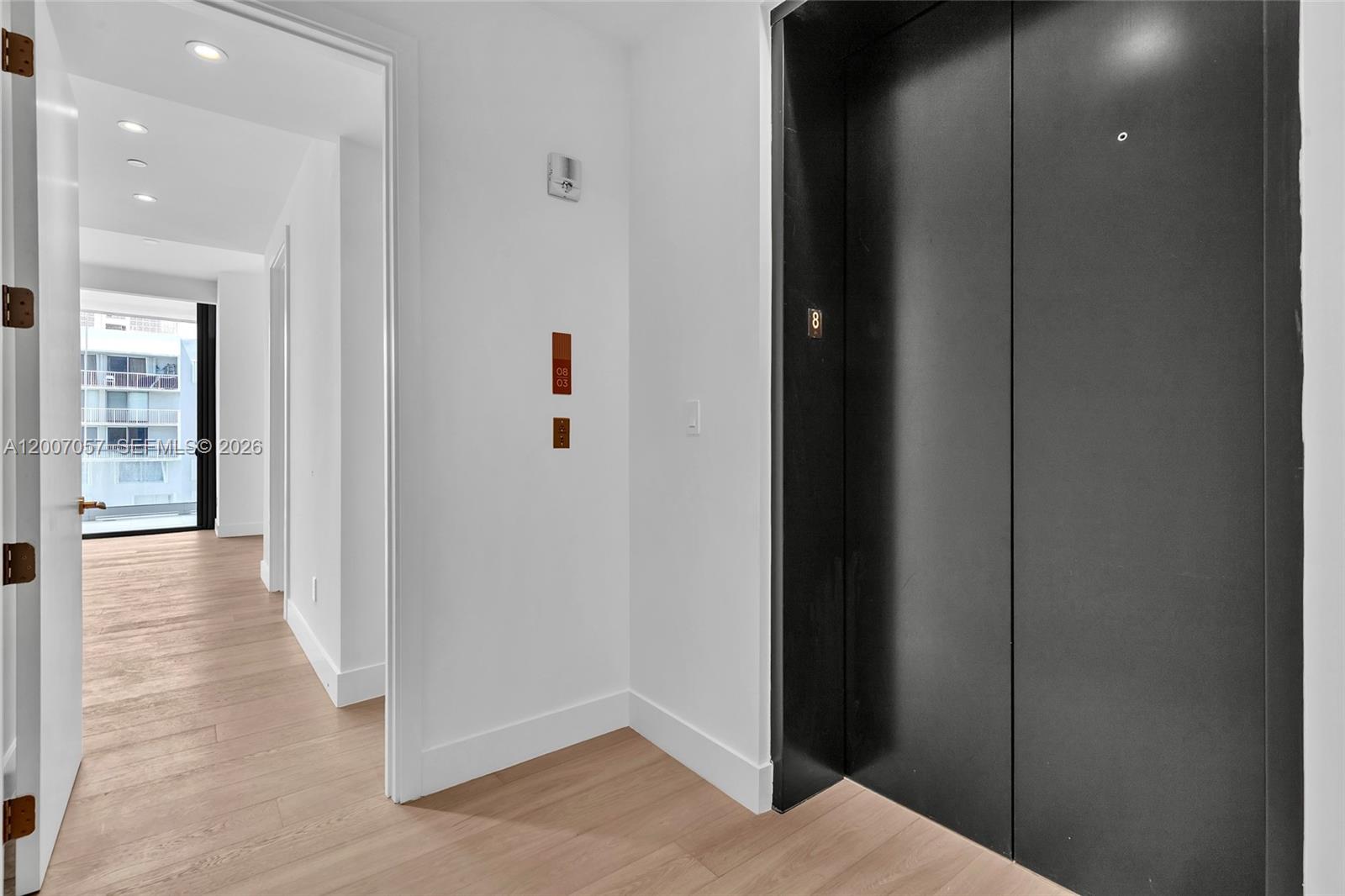 A hallway with light wood flooring leads to a balcony, adjacent to a black elevator door — 175 SE 25 Road # 803, Miami FL 33129, MIAMI, FL
