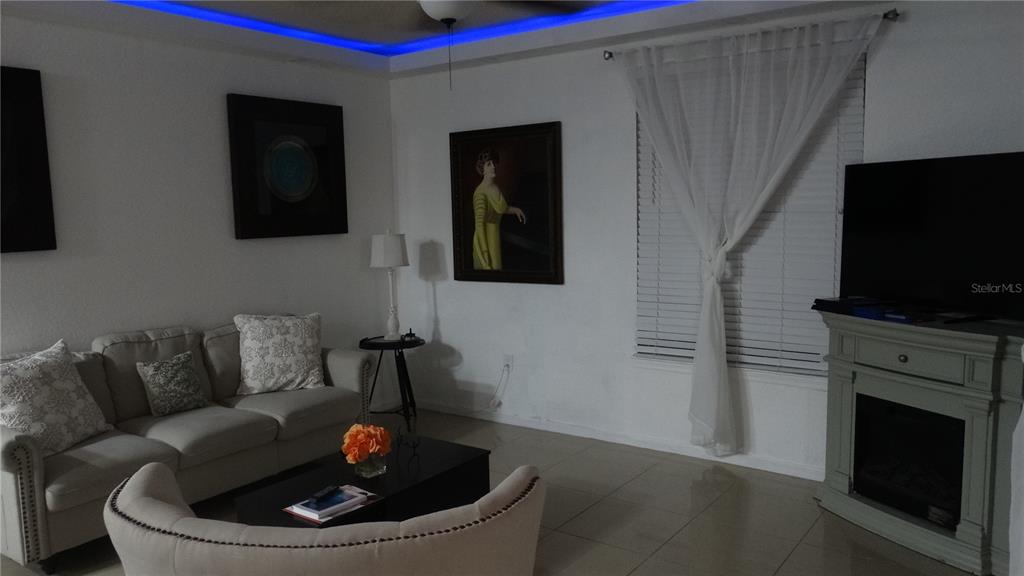 A living room features a beige sofa, a fireplace with a television, and blue ceiling lighting — 5957 WESTGATE DRIVE UNIT 1914, ORLANDO, FL