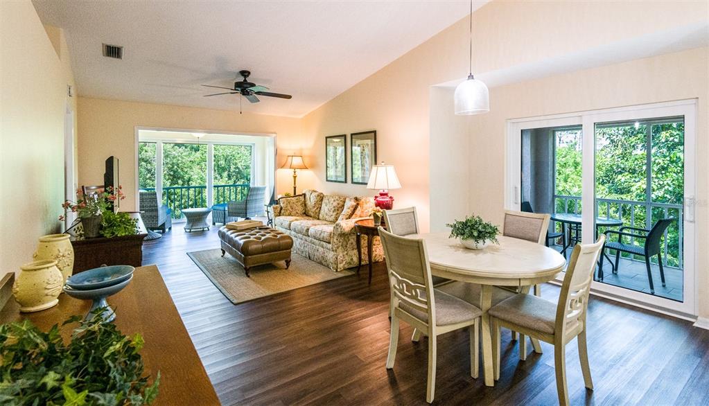 An open-concept living and dining area features wood-look flooring, vaulted ceilings, and sliding glass doors — 5658 SHEFFIELD GREENE CIRCLE UNIT 66-17, SARASOTA, FL