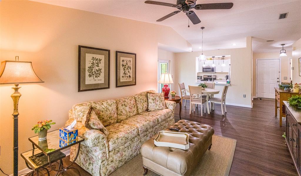 A living room with a floral sofa, leather ottoman, and an adjacent dining area — 5658 SHEFFIELD GREENE CIRCLE UNIT 66-17, SARASOTA, FL