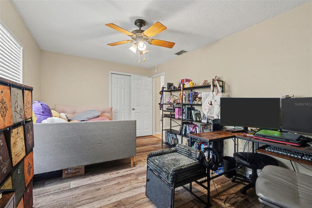 A bedroom features wood-look flooring, a ceiling fan, a gray bed, and a computer desk — 412 W IDLEWILD AVENUE, TAMPA, FL