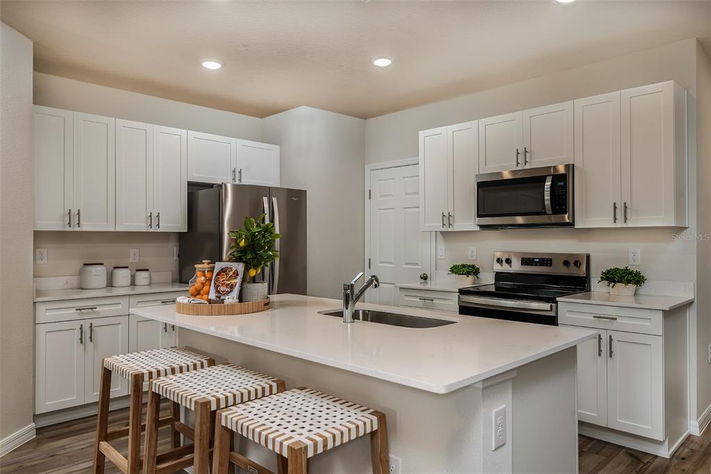 A modern kitchen features white cabinets, stainless steel appliances, and a central island with seating — 9902 PELICAN COAST DRIVE, DADE CITY, FL