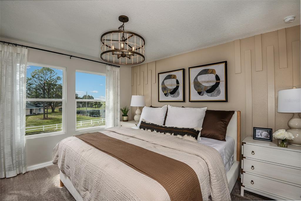 A bedroom features a bed with brown bedding, a chandelier, and a paneled accent wall — 9902 PELICAN COAST DRIVE, DADE CITY, FL