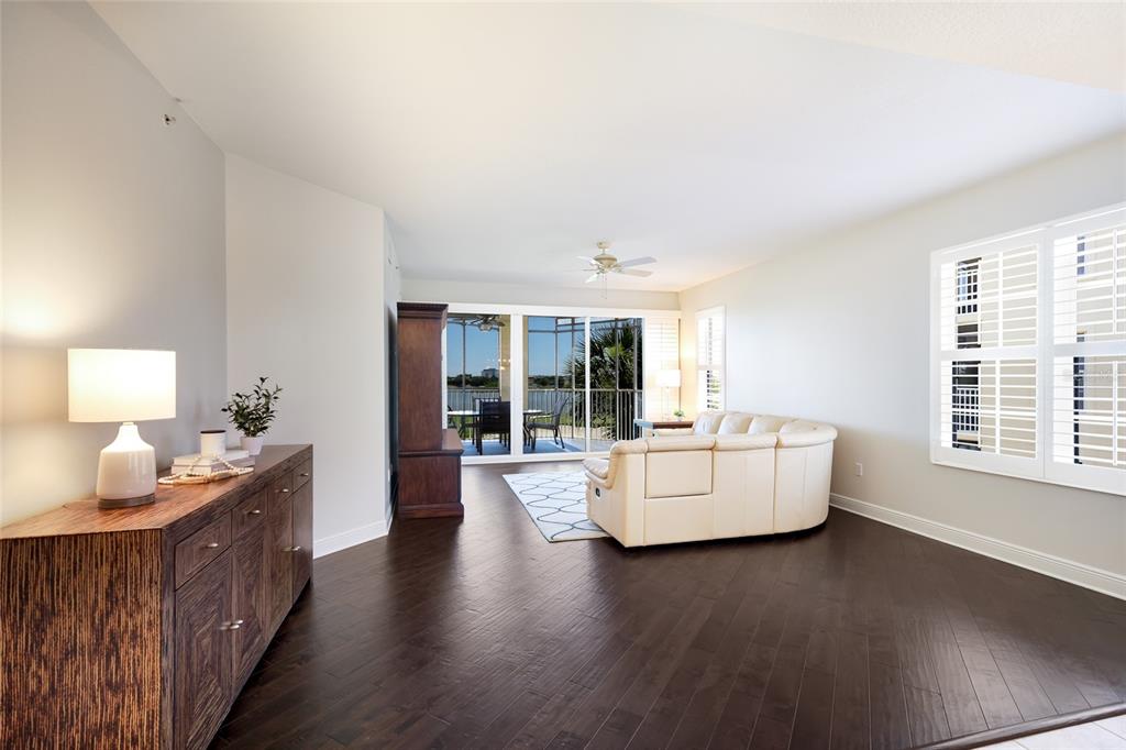 A living room features dark hardwood floors, a white leather sofa, and a balcony view — 6422 WATERCREST WAY UNIT 302, LAKEWOOD RANCH, FL