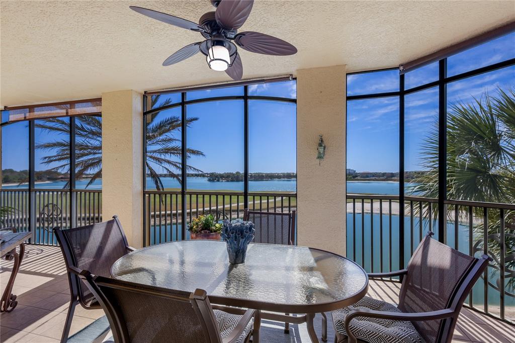 A screened-in balcony with a dining set, ceiling fan, and views of a lake — 6422 WATERCREST WAY UNIT 302, LAKEWOOD RANCH, FL