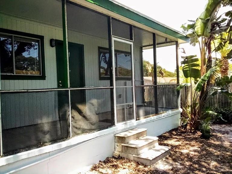 A screened-in porch with concrete steps sits beside a large plant in a yard — 10530 68TH AVENUE, SEMINOLE, FL