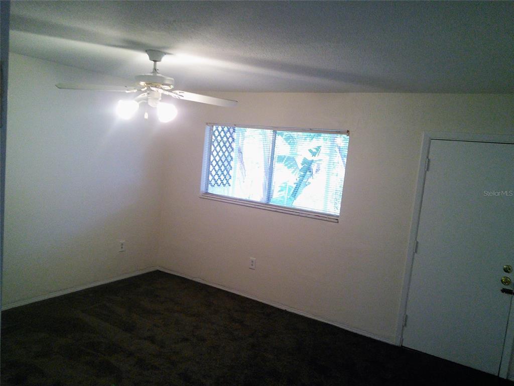 An empty bedroom features dark carpeting, a ceiling fan, a window, and a white door — 10530 68TH AVENUE, SEMINOLE, FL