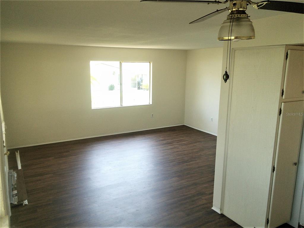 An empty room features dark wood-look flooring, light-colored walls, a ceiling fan, and a window — 10530 68TH AVENUE, SEMINOLE, FL