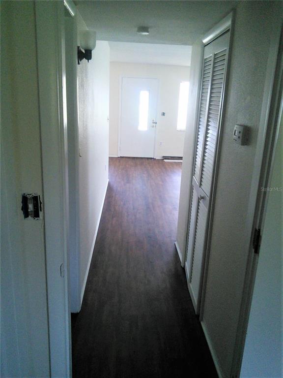 A hallway with dark wood-look flooring leads to an exterior door in a bright room — 10530 68TH AVENUE, SEMINOLE, FL