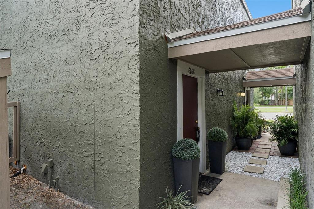 An exterior view of a building entrance with a covered walkway and potted plants — 6168 PEREGRINE AVENUE UNIT 12B, ORLANDO, FL