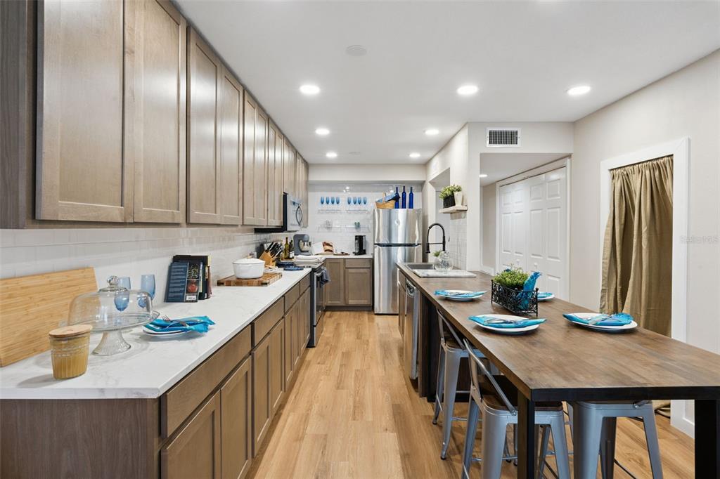 A galley-style kitchen features wood cabinets, white countertops, a long wooden island, and stainless appliances — 6168 PEREGRINE AVENUE UNIT 12B, ORLANDO, FL