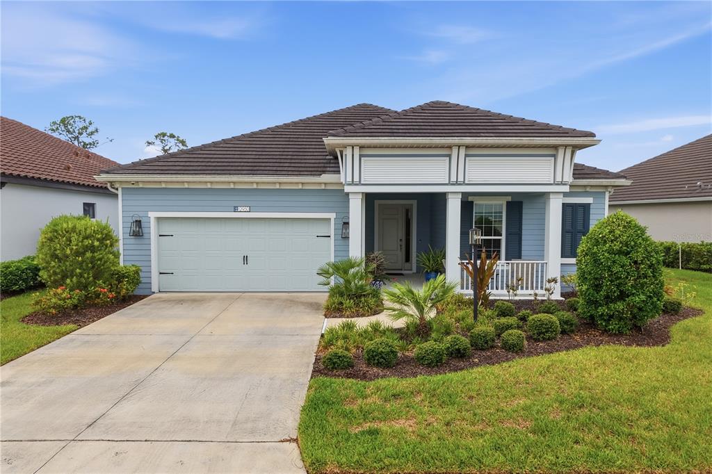 A blue single-story house features a two-car garage, a covered front porch, and landscaped yard — 12950 SEASONG TERRACE, BRADENTON, FL