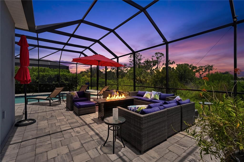 A screened-in patio features a fire pit, outdoor sectional seating, and a swimming pool at sunset — 12950 SEASONG TERRACE, BRADENTON, FL