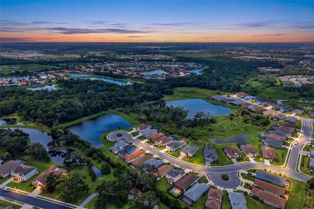 An aerial view shows a suburban neighborhood with houses surrounding several ponds at sunset — 12950 SEASONG TERRACE, BRADENTON, FL