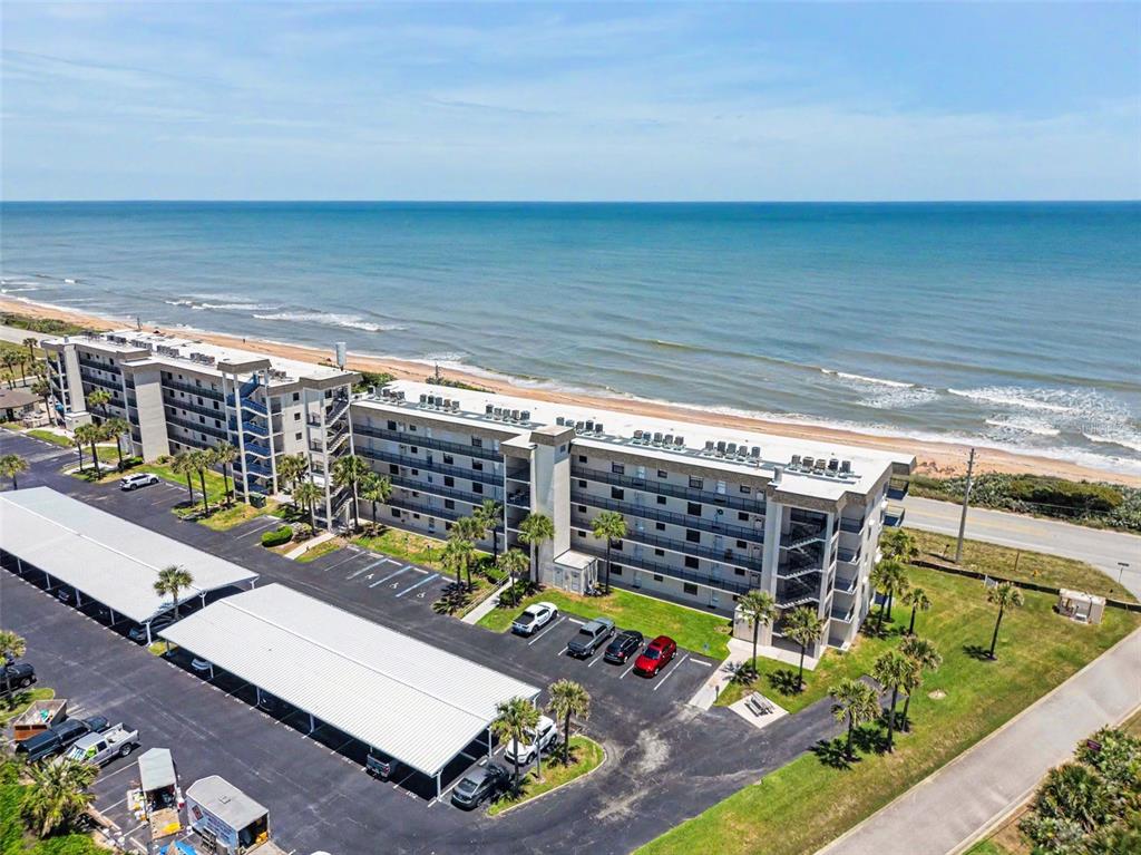 An aerial view of a multi-story beachfront apartment complex with a parking lot and carports — 3100 OCEAN SHORE BOULEVARD UNIT 101, ORMOND BEACH, FL