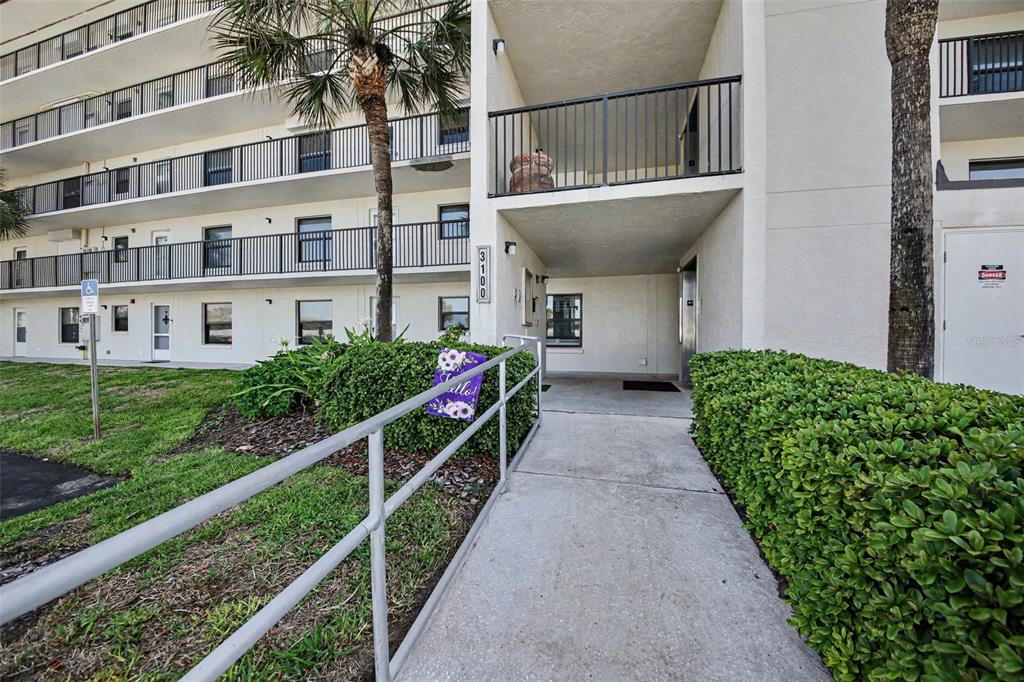 A concrete walkway leads to the entrance of a multi-story apartment building with balconies — 3100 OCEAN SHORE BOULEVARD UNIT 101, ORMOND BEACH, FL
