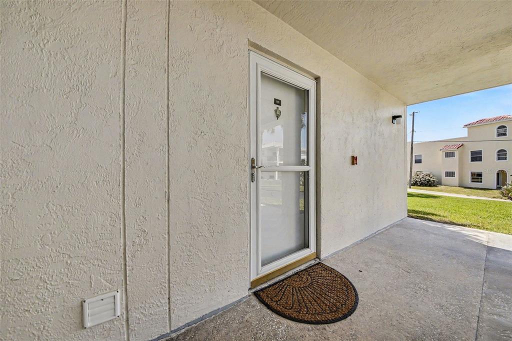 A white storm door leads to an entryway with a concrete floor and textured walls — 3100 OCEAN SHORE BOULEVARD UNIT 101, ORMOND BEACH, FL
