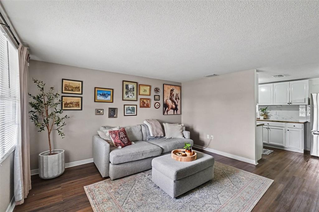 A living room with a gray sofa, ottoman, gallery wall, and an adjacent white kitchen — 1611 SMITHFIELD CIRCLE W, LAKELAND, FL