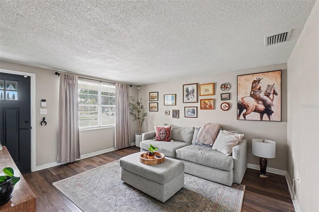 A living room features a gray sectional sofa, an ottoman, and a gallery wall — 1611 SMITHFIELD CIRCLE W, LAKELAND, FL