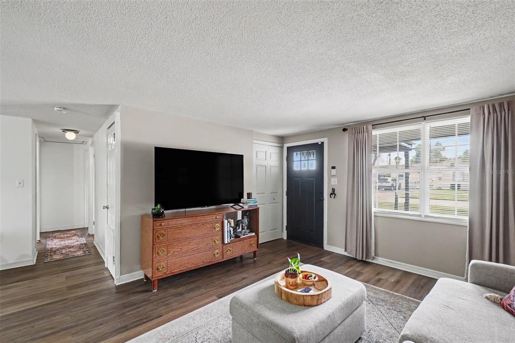 A living room features wood-look flooring, a television on a wooden dresser, and a front door — 1611 SMITHFIELD CIRCLE W, LAKELAND, FL