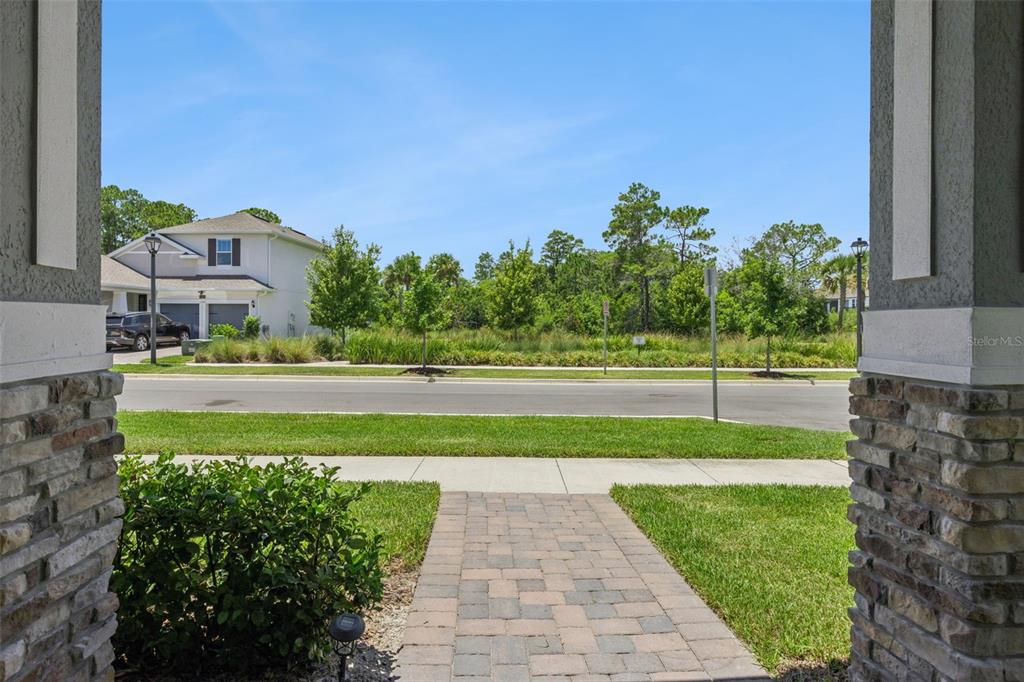 A view from a stone-columned porch looking out toward a street, lawn, and wooded area — 13253 PEACEFUL MELODY DRIVE, WINTER GARDEN, FL