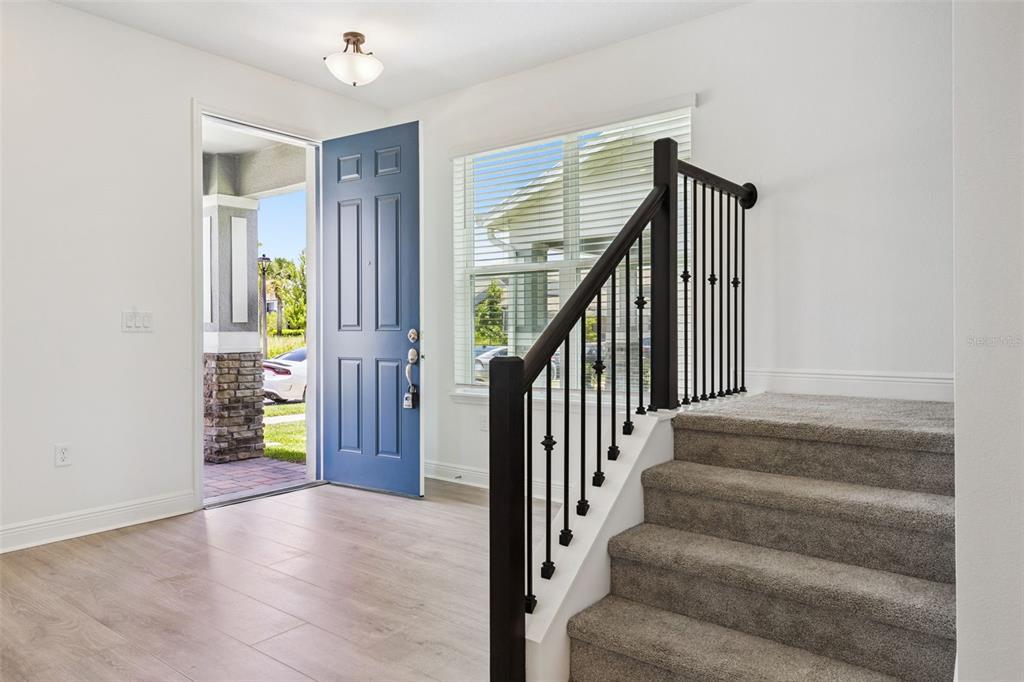 An entryway features a blue front door, light wood flooring, and carpeted stairs with railings — 13253 PEACEFUL MELODY DRIVE, WINTER GARDEN, FL