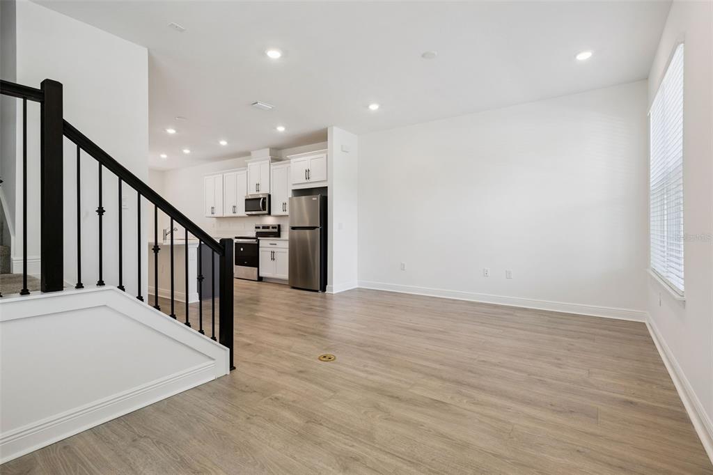 A bright, open-concept living area features light wood-look flooring, white walls, and a modern kitchen — 13253 PEACEFUL MELODY DRIVE, WINTER GARDEN, FL