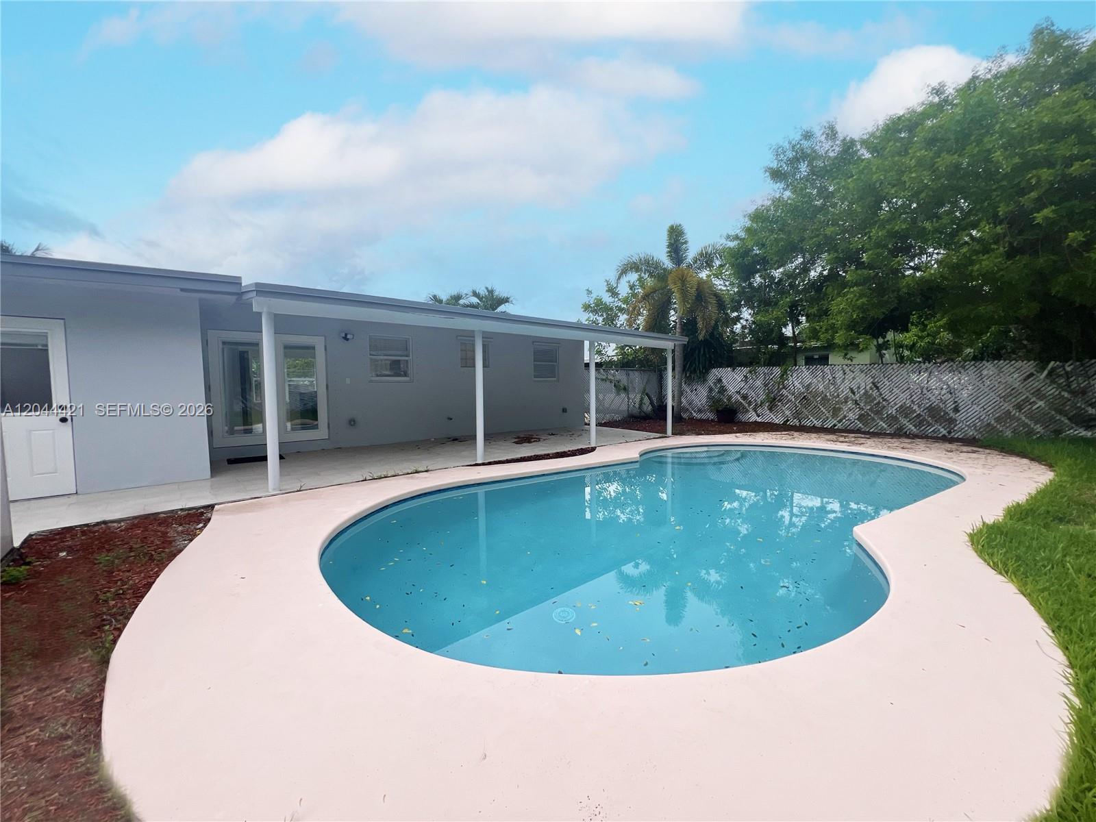 A backyard features a kidney-shaped swimming pool, a covered patio, and a white lattice fence — 2679 NW 57th Ter, Margate FL 33063, MARGATE, FL